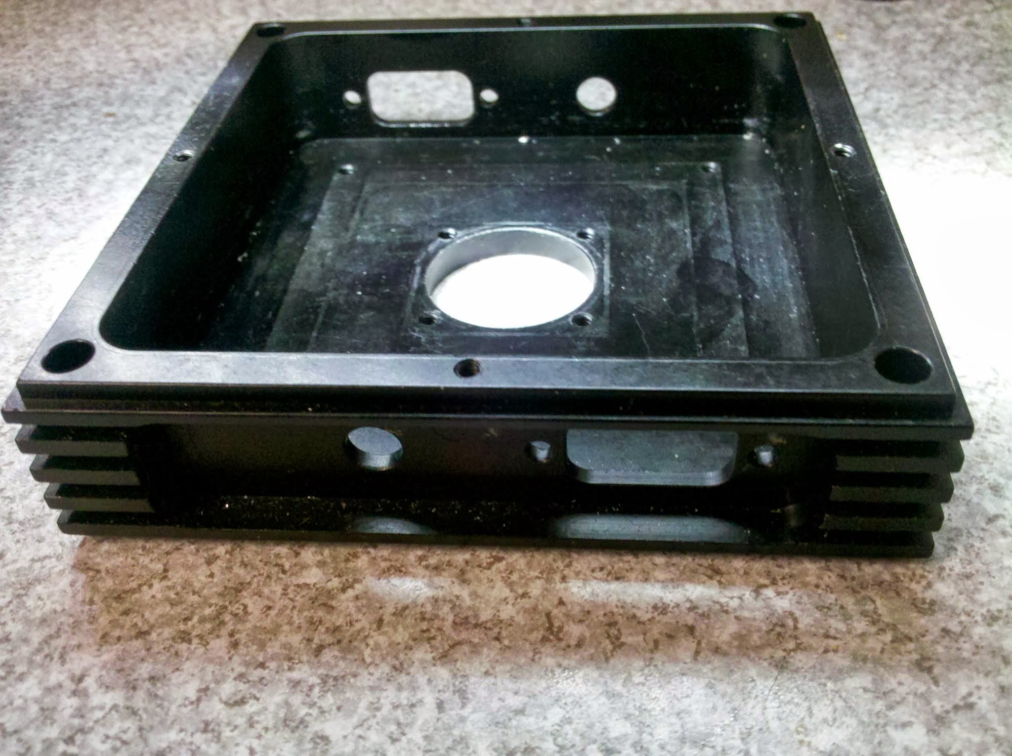 Black anodised finned aluminium enclosure with a recessed pocket and machined central bore